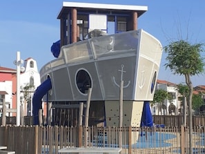 A play structure resembling a ship with a slide, surrounded by a fence.