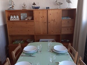 A dining area with a table set for four, wooden cabinets with decorative items, and a view of the outside.