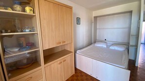A bedroom with a bed, a wardrobe, and a shelf with kitchen items. - Seaside studio for 3 pers with parking (Port Leucate)