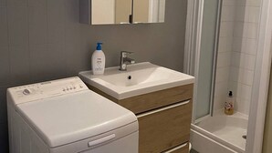 A bathroom with a washing machine, a sink, and a shower.