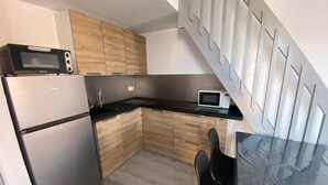A compact kitchen with a refrigerator, microwave, and stove. It features wooden cabinets and a black countertop.