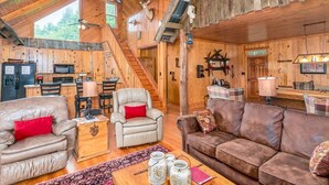 Interno rustico di una baita con cucina, zona pranzo e soggiorno arredato con divani in pelle e un tavolino in legno.