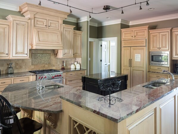 A kitchen with light wood cabinets, a granite countertop, a stove, and a microwave.