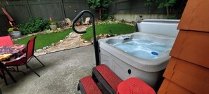 A hot tub with a stone pathway leading to a patio area with chairs and a table.