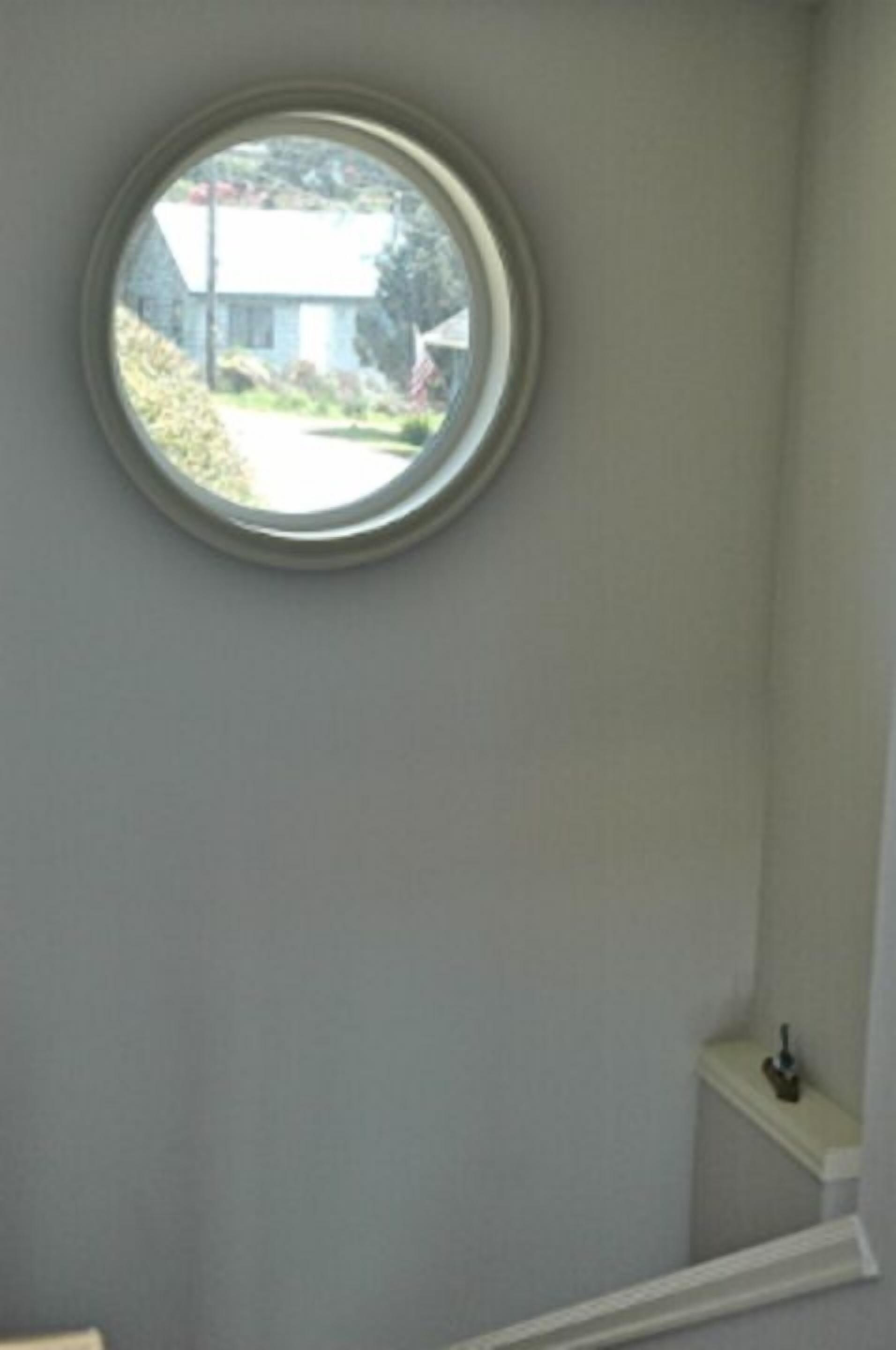 A bathroom with a round window, a white sink, and a small shelf with a bottle.