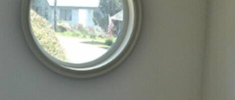 A bathroom with a round window, a white sink, and a small shelf with a bottle.