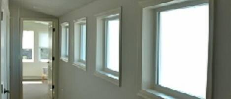A hallway with multiple windows, carpeted floor, and a door at the end leading to another room.