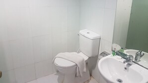 A small bathroom with a toilet, sink, and mirror. - PIH Batam (Batam)