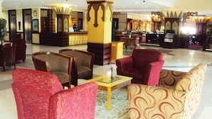 A lobby with red and patterned sofas, wooden chairs, a reception desk, and decorative pillars. - PIH Batam (Batam)