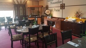 A restaurant with round tables and chairs, a buffet area with a yellow tablecloth, and decorative wall elements. - PIH Batam (Batam)