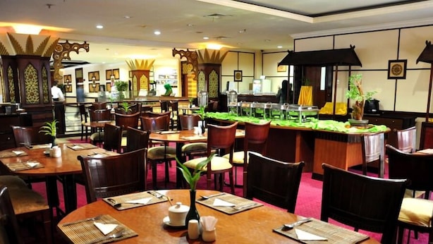 A restaurant with multiple dining tables and chairs, some with plants on the tables. - PIH Batam (Batam)