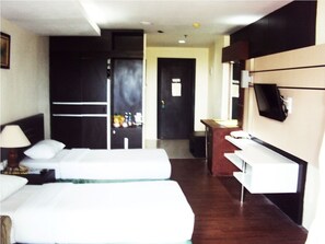 Habitación de hotel con dos camas, un escritorio, un televisor y una puerta que da a un pasillo.