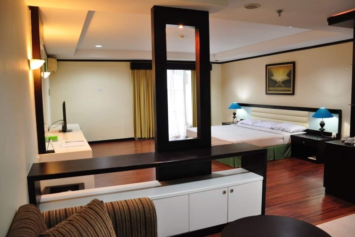 A hotel room with a bed, bedside tables, a desk, a chair, a sofa, and a large mirror.