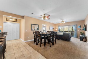A dining area with a round table and chairs, a sofa, a ceiling fan, and a large window with curtains. - Spacious Lake Front Condo, Sunsets, 5 min to SDC (Branson)