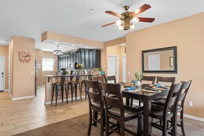 A dining area with a table set for four, a ceiling fan, and a kitchen in the background. - Spacious Lake Front Condo, Sunsets, 5 min to SDC (Branson)