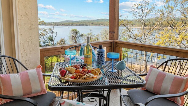 Ein Balkon mit gedecktem Tisch, mit Blick auf einen See, Bäume und Hügel im Hintergrund.