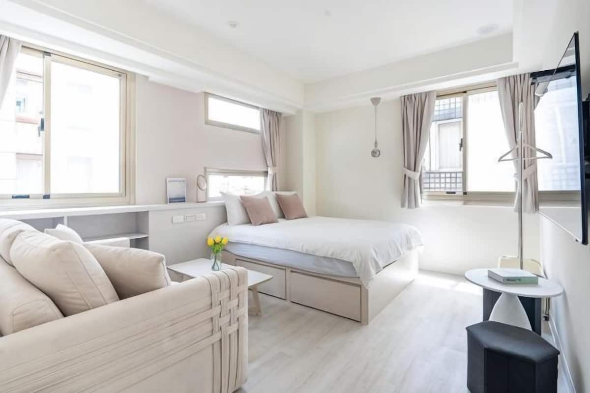 A modern hotel room with a bed, a sofa, a desk, and a small table.