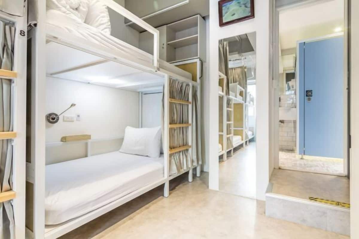 A bunk bed room with a white mattress, wooden headboard, and a small bedside table. There are built-in shelves with storage space and a blue door leading to another room.