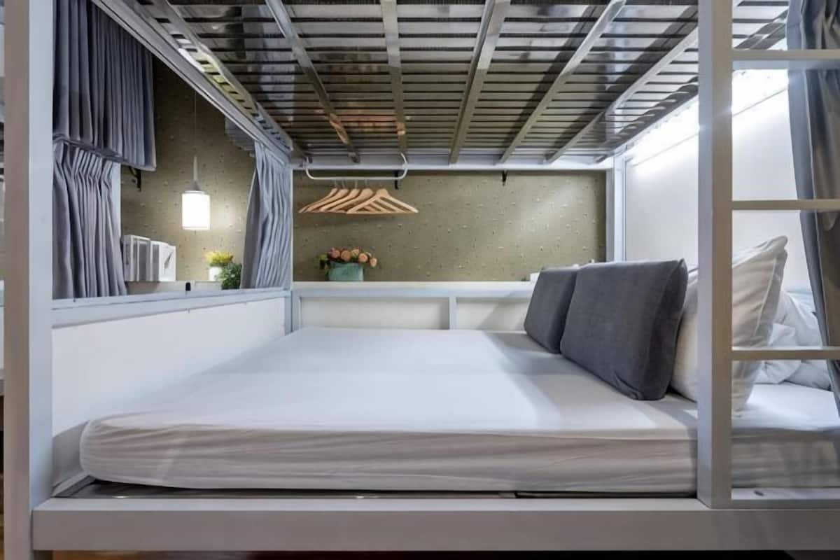A bunk bed with a mattress, a hanging light fixture, a wall-mounted shelf with a plant, and a window with curtains.