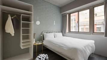 A bedroom with a bed, a wardrobe, a small table, and a window.