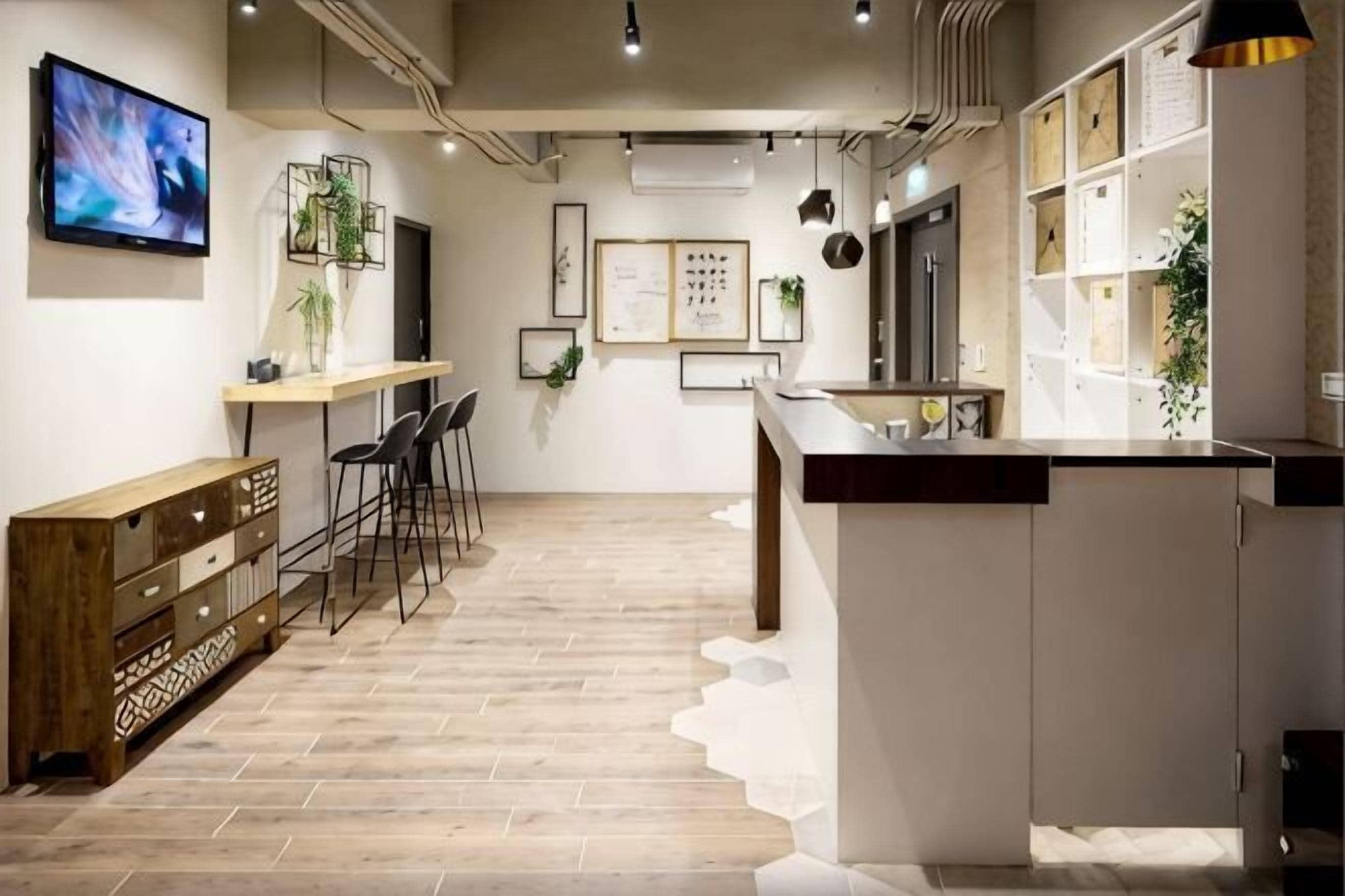 A modern kitchen with a wooden floor, bar stools, a long counter, and a TV mounted on the wall.