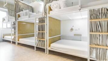 A row of bunk beds with storage shelves, a window with curtains, and a wall-mounted light fixture.