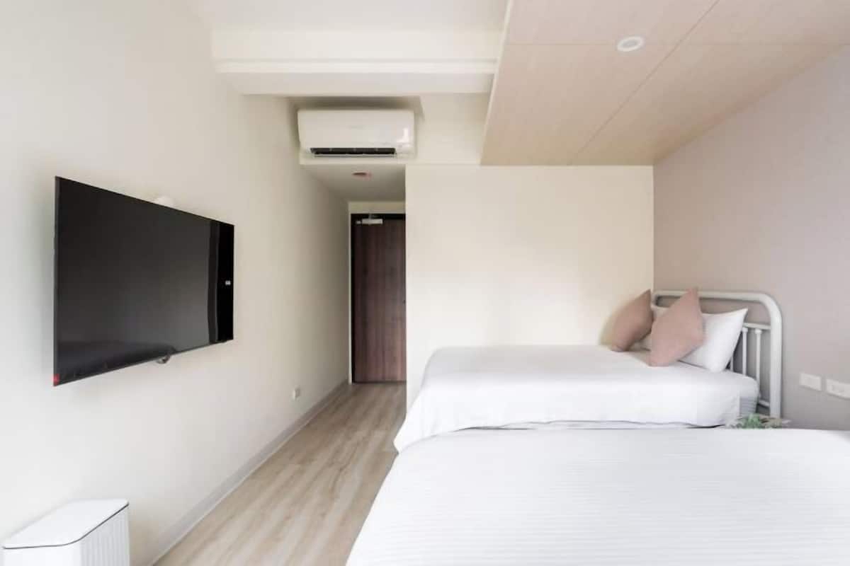 A modern hotel room with a flat-screen TV mounted on the wall, a bed with white bedding and two pillows, and a small radiator on the floor.