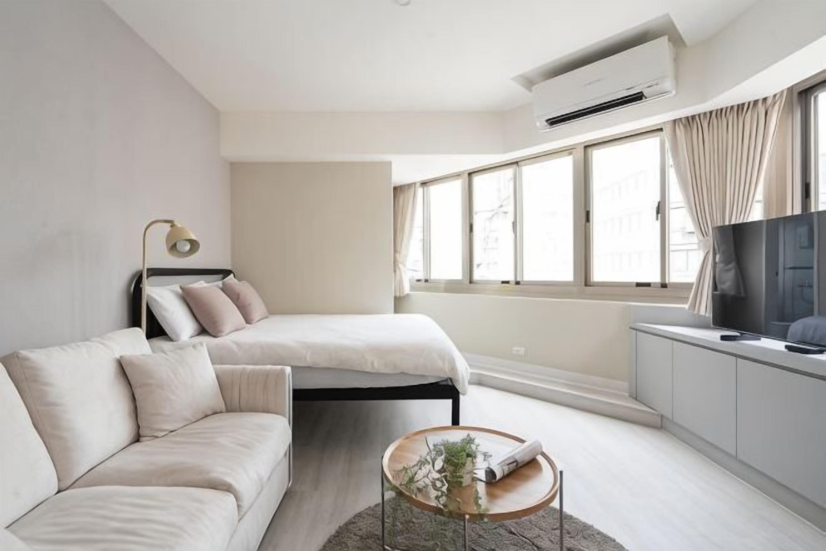 A modern bedroom with a bed, a sofa, a TV, and a window.