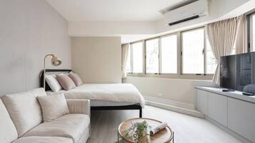 A modern bedroom with a bed, a sofa, a TV, and a window.
