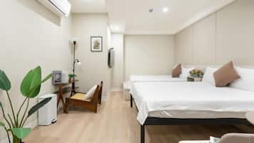 A modern hotel room with a large bed, a desk, and a chair. There is a potted plant and a wall-mounted air conditioner.