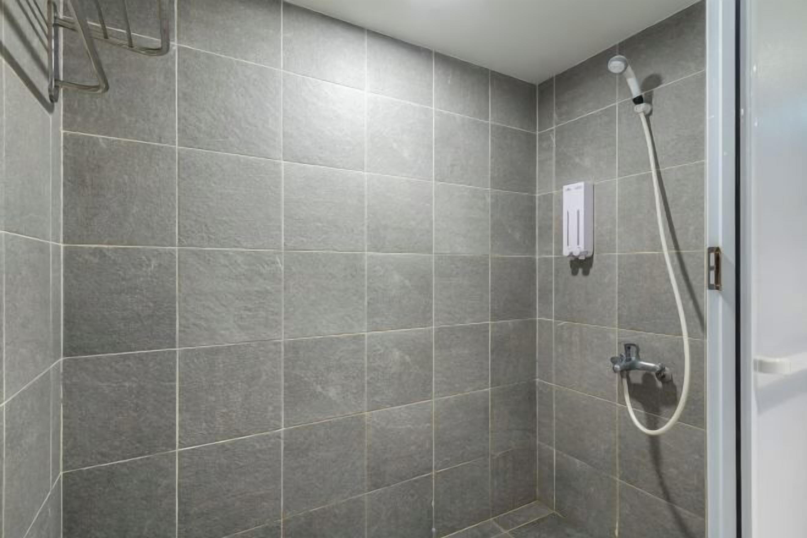 A shower area with grey tiles and a handheld showerhead.