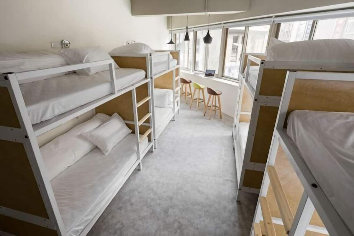 A bunk bed room with a desk and chairs, large windows, and a carpeted floor.