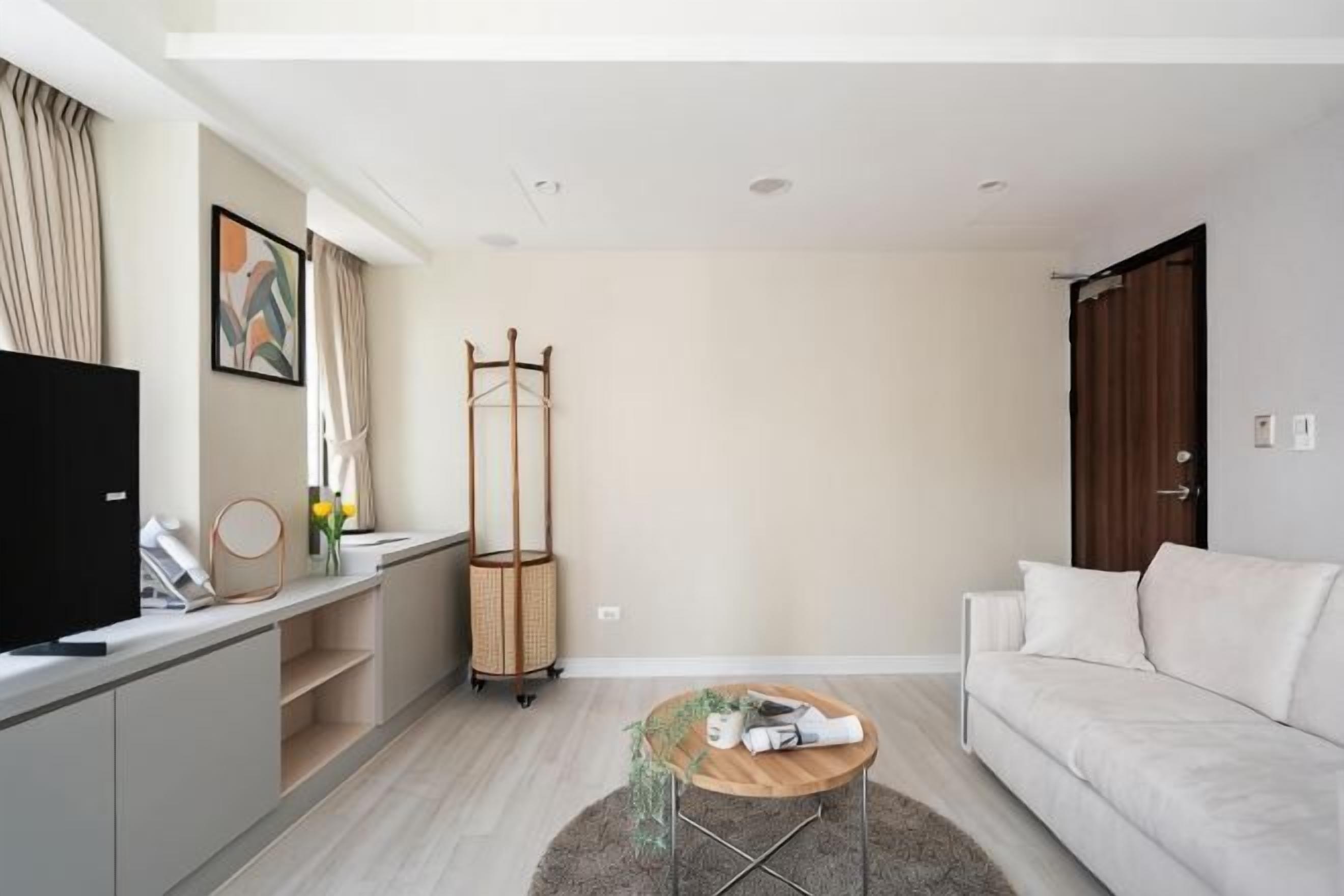 A modern living room with a sofa, a coffee table, a TV, a TV stand, a coat rack, and a window with curtains.