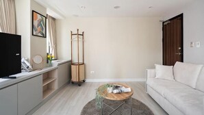 A modern living room with a sofa, a coffee table, a TV, a TV stand, a coat rack, and a window with curtains. - 109 Inn Taipei (Taipei City)