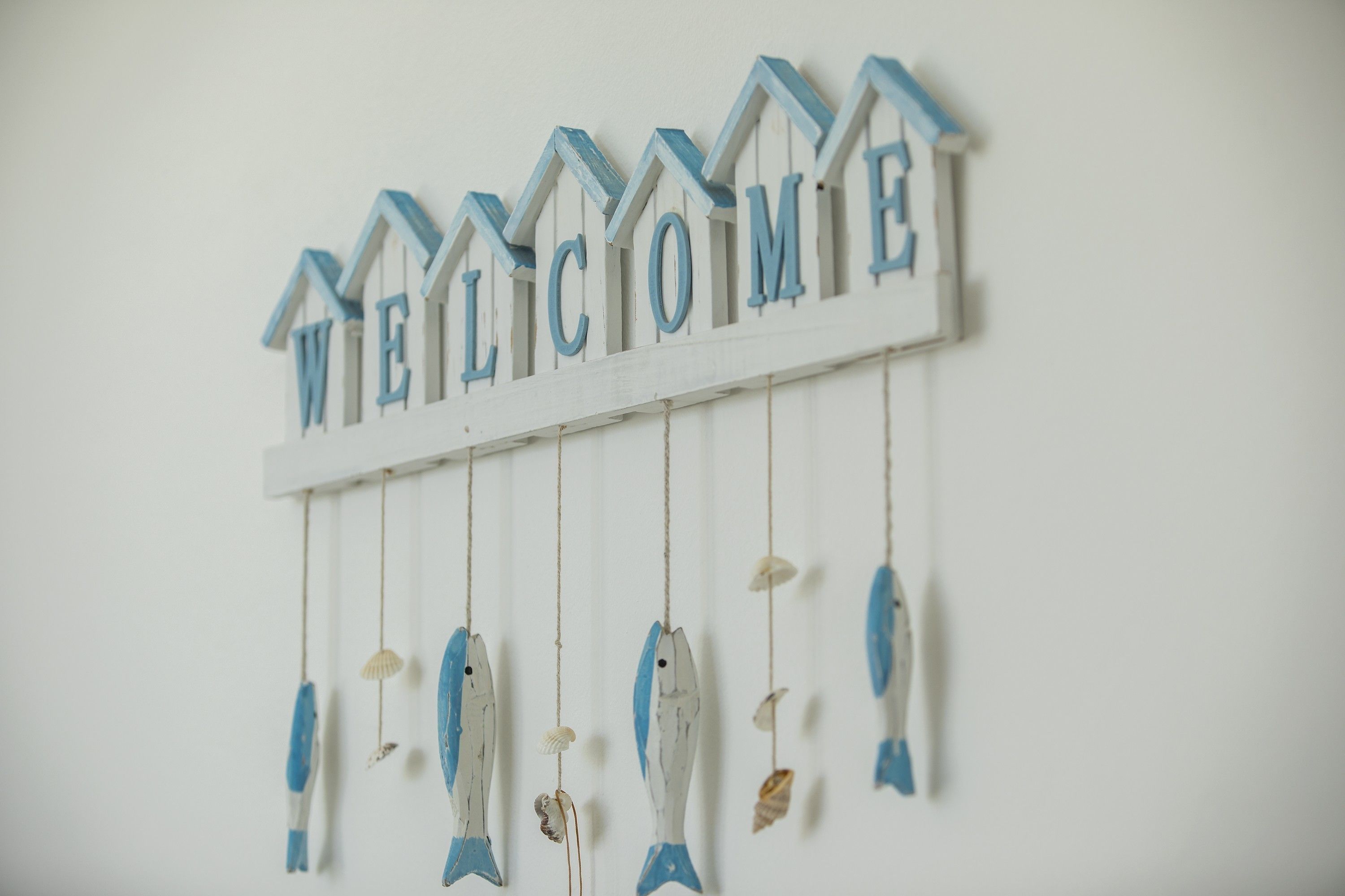 A wall decoration with the word "WELCOME" in blue letters, hanging from a white base with blue accents, and several fish-shaped ornaments below.