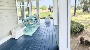 A porch with a table and chairs, a white trash bin, and a view of a golf course.