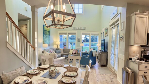 A spacious living room with a large round table set for dining, a cozy seating area with a sofa and chairs, and a kitchen area with a TV and cabinets.