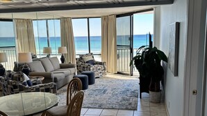 A spacious living area with a large glass table, comfortable seating, and a view of the ocean.