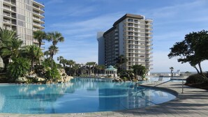 A swimming pool with a paved deck, surrounded by palm trees and a view of a high-rise building.