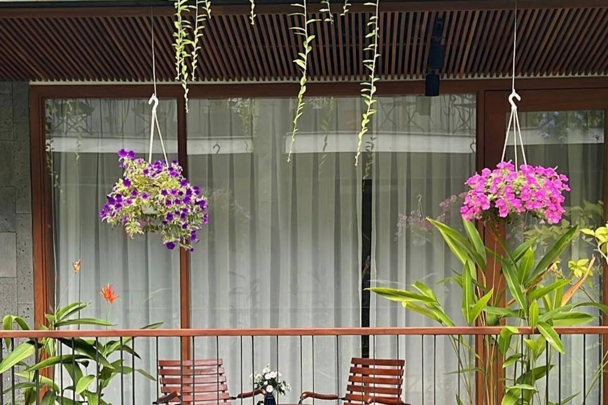 Un balcón con dos sillas de madera, una mesita redonda y cestas de flores colgantes.