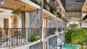 Ein mehrgeschossiges Atrium mit einer zentralen Wasserspiele, Balkonen mit Pflanzen und moderner Möblierung.