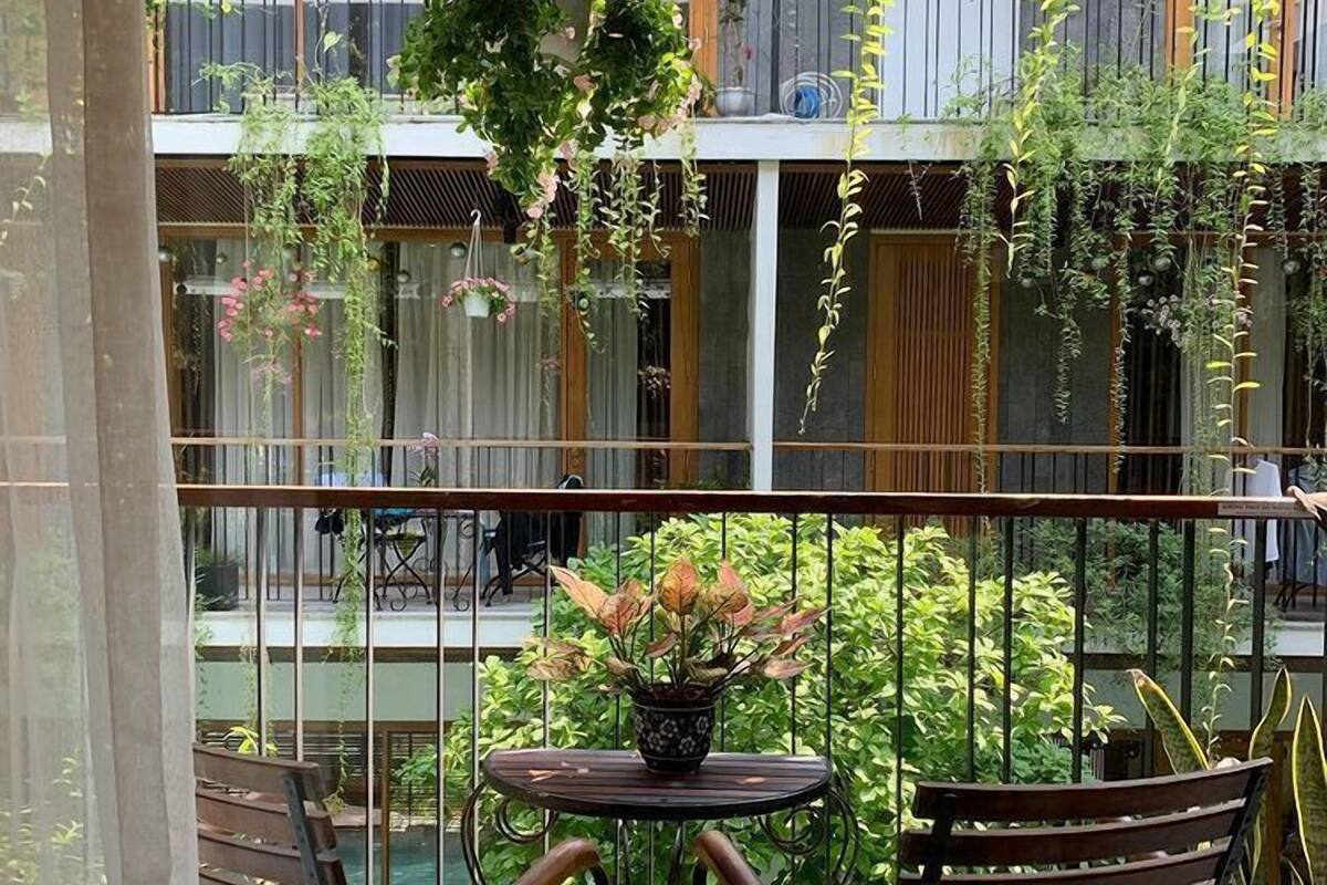 Balcón con mesa y dos sillas, rodeado de plantas colgantes y vista al interior del edificio.