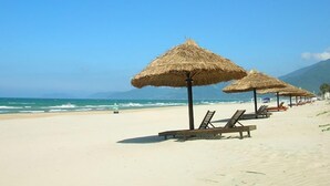 Ein Strand mit reetgedeckten Sonnenschirmen und Liegestühlen.