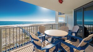 Ein Balkon mit Blick auf den Strand, einem runden Tisch und blauen Stühlen.