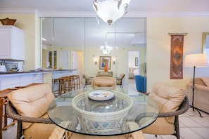 Una sala de estar con una mesa de vidrio, sillas de mimbre, un sofá, una lámpara y una cocina al fondo.