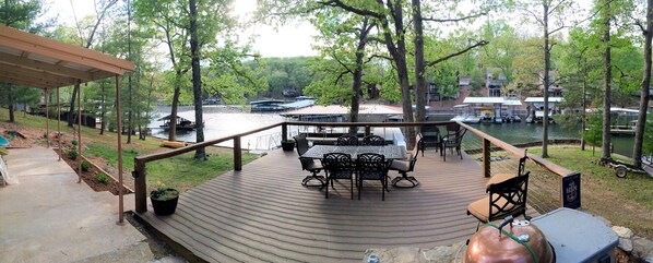 A wooden deck with outdoor furniture, overlooking a river with boats and docked yachts.