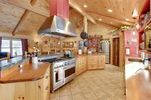 Enjoy cooking in this well-equipped kitchen with a central island, stainless steel stove, and oven, surrounded by wooden cabinetry and a high ceiling.