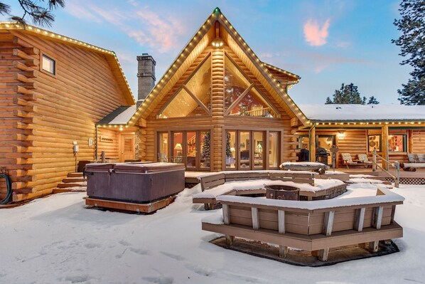 Cozy cabin with a fireplace, hot tub, and deck, surrounded by snow.