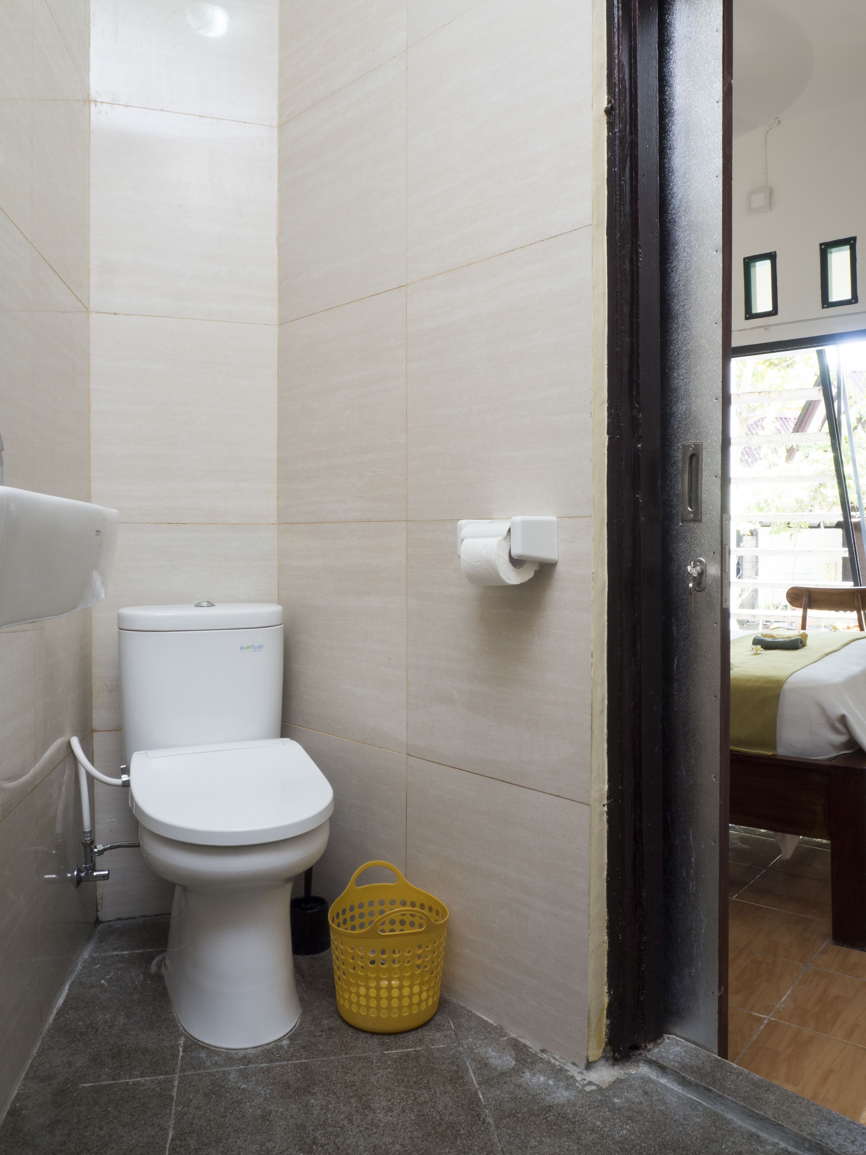 A bathroom with a toilet, a yellow basket, and a toilet paper holder.