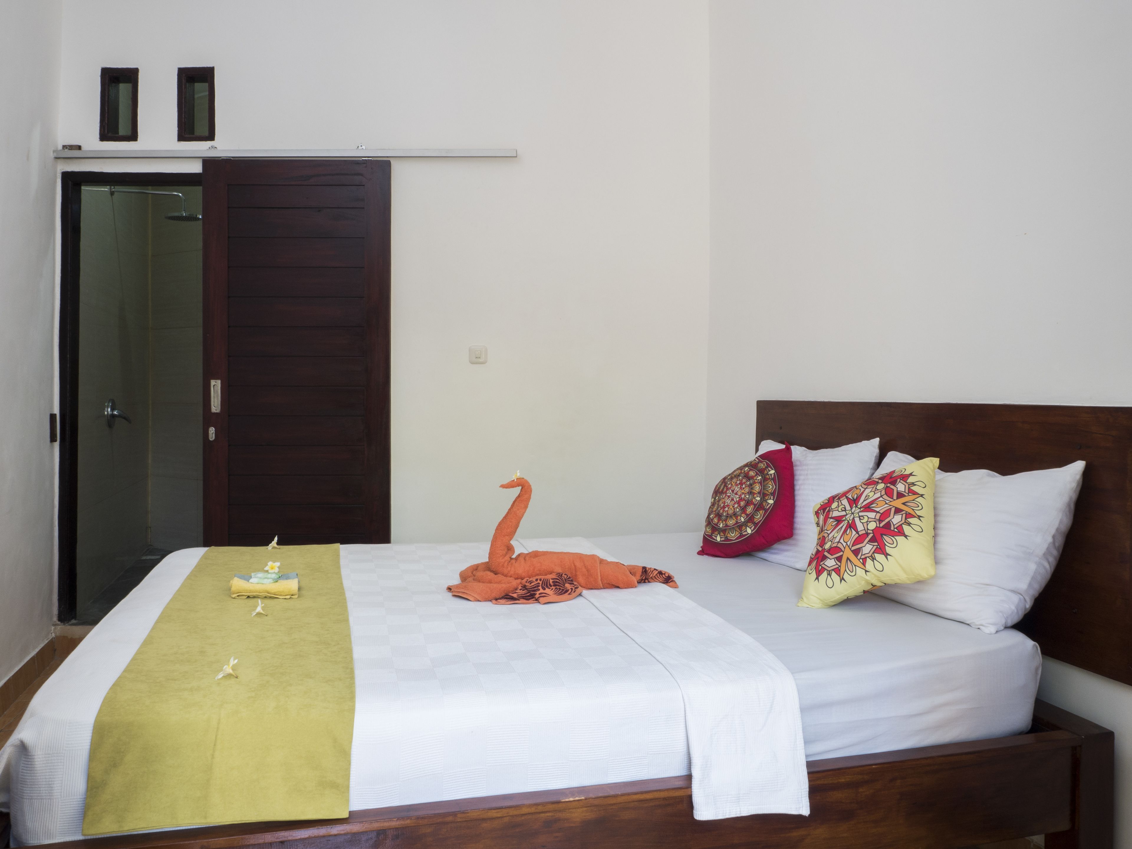 A neatly made bed with a decorative swan pillow, a wooden headboard, and a green towel.